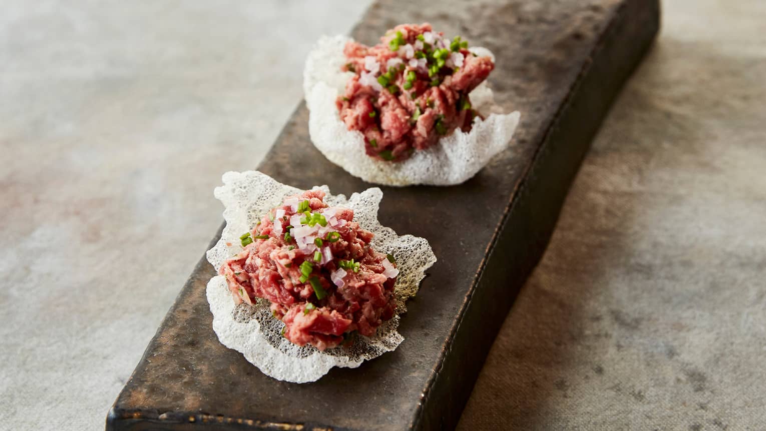 Steak tartare served in white shells on a marble countertop. 