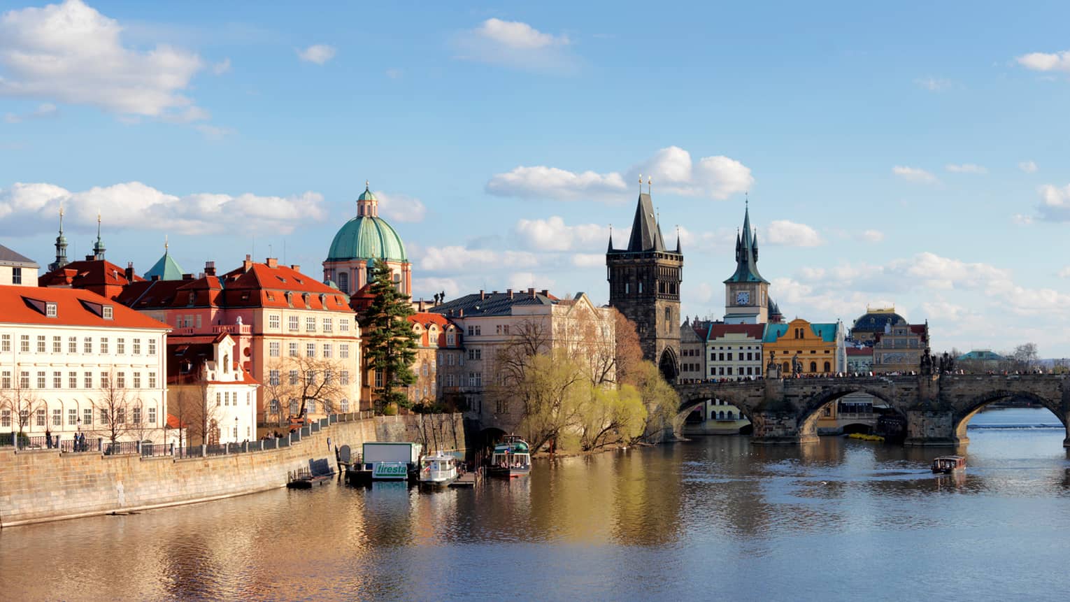 Prague waterfront on sunny day with historic Charles Bridge crossing Vltava River