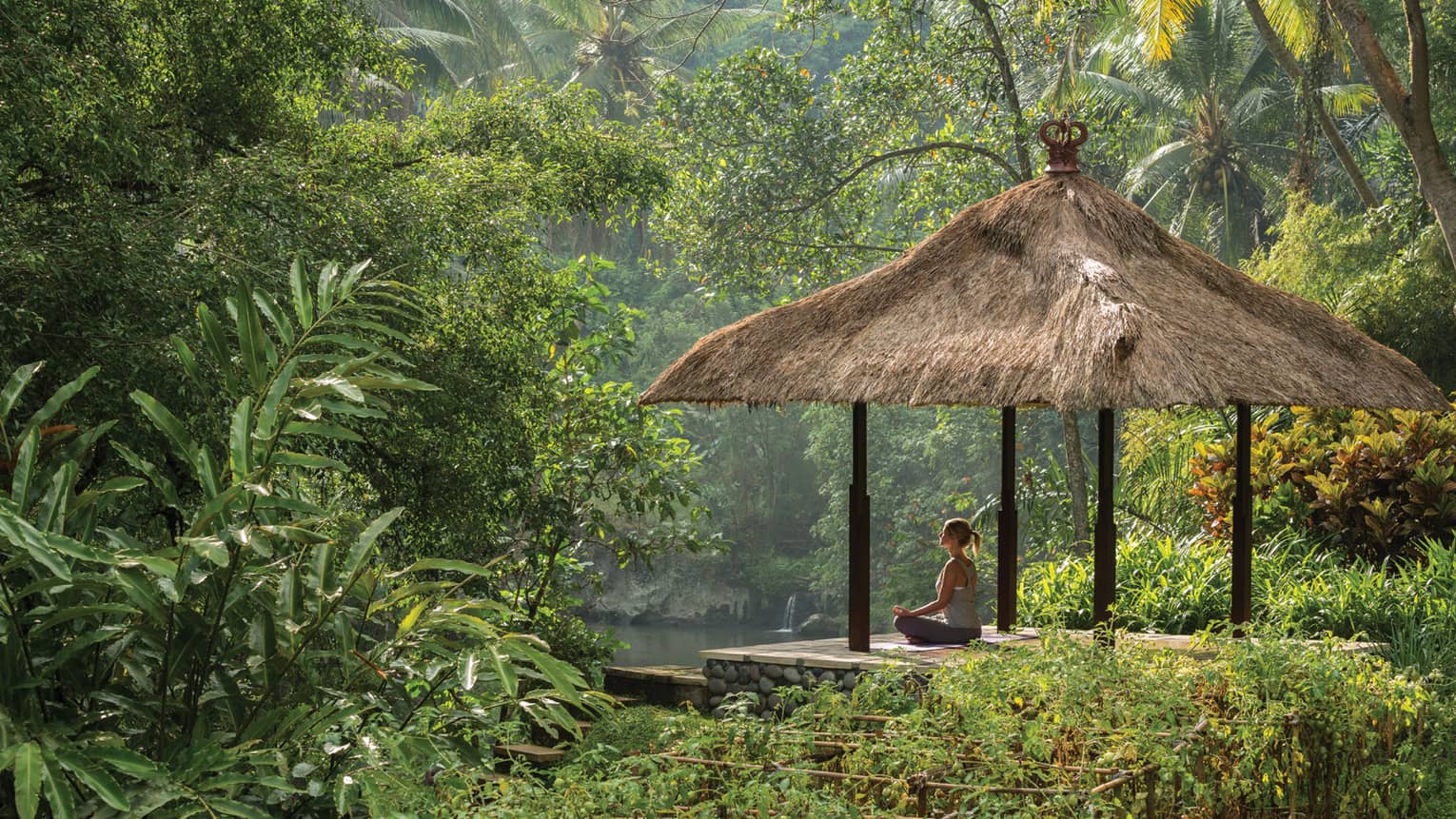 Woman meditating on pavilion hut by the Ayung River in Bali