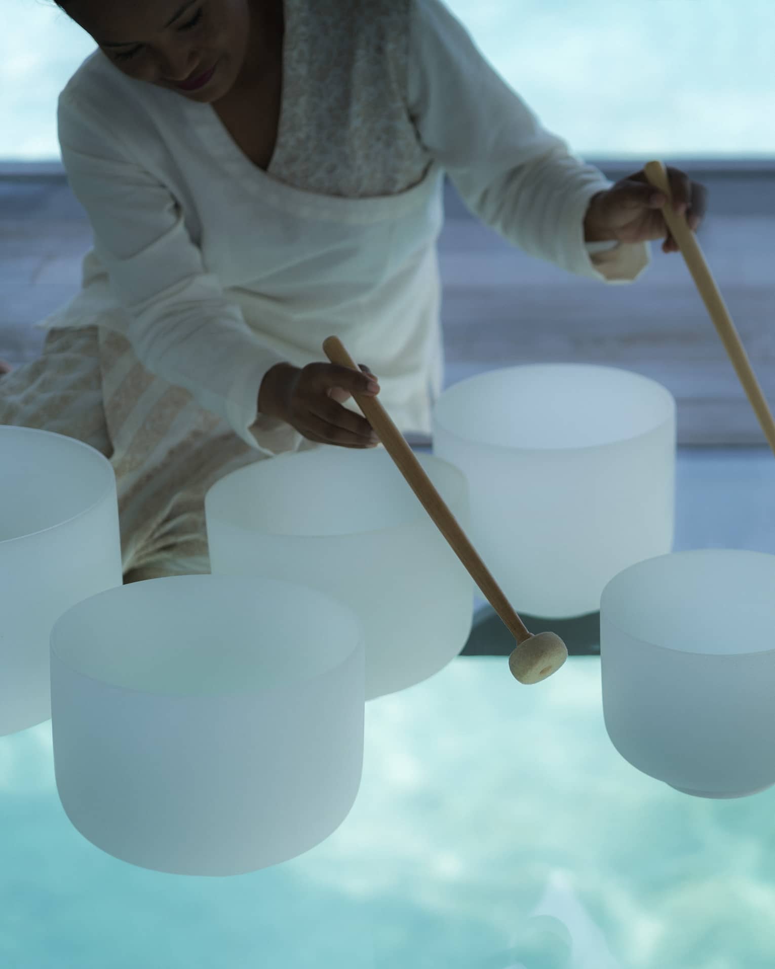 Spa staff plays various white crystal bowls with wood mallets during sound healing session