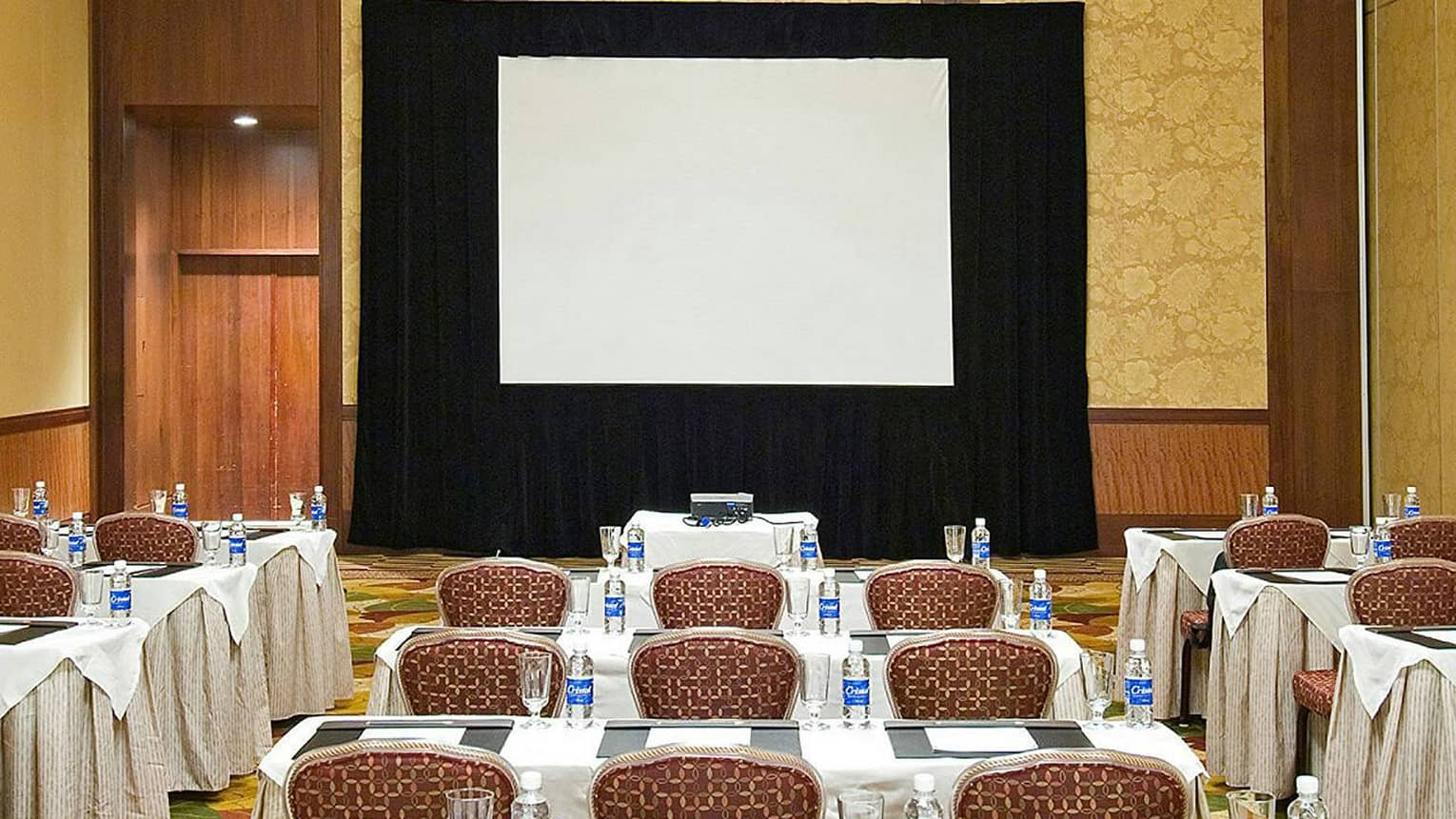 Rows of meeting chairs, tables facing large screen in Guanacaste ballroom