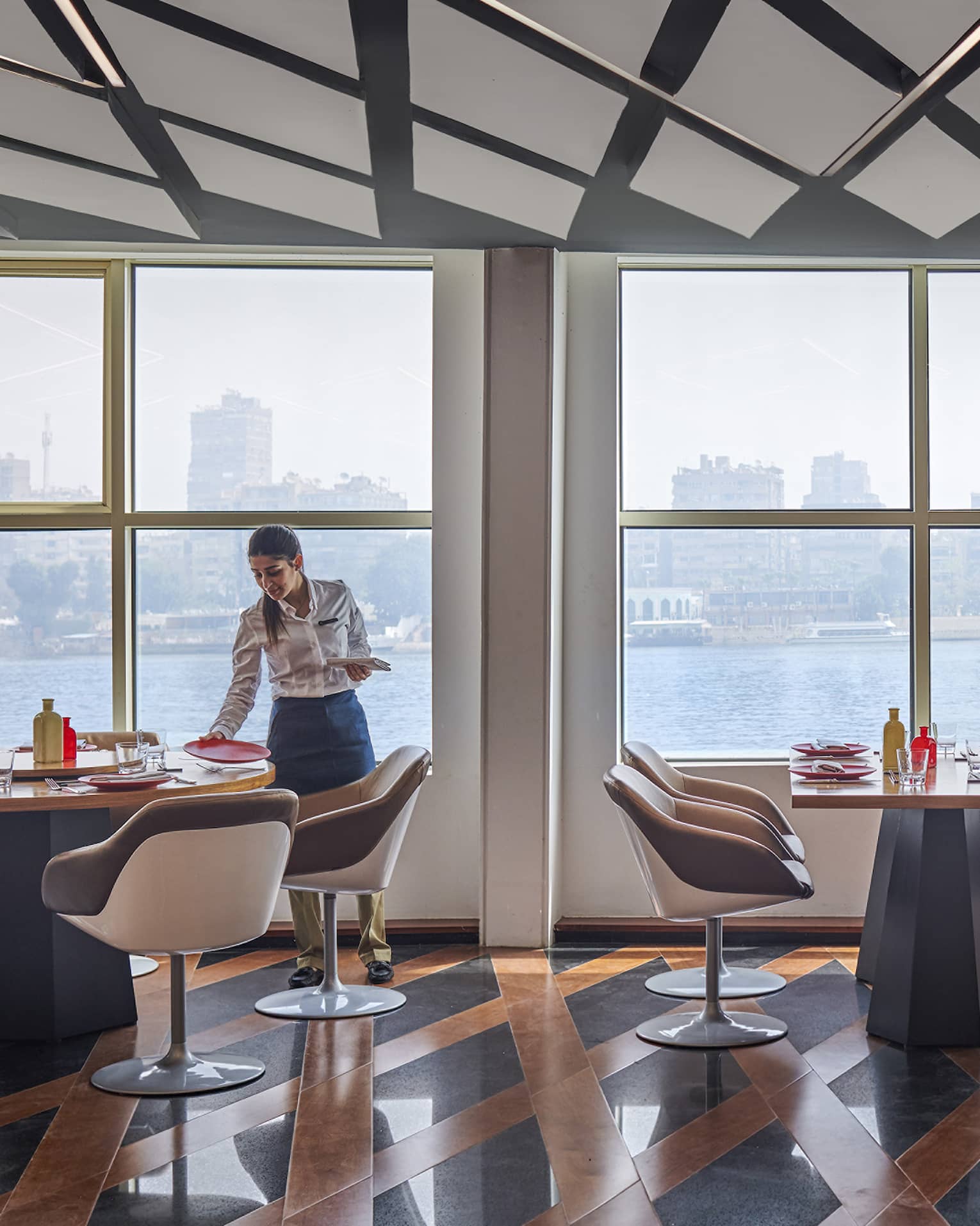 Contemporary restaurant with server on left, rectangular tables, lattice floor, Nile River views