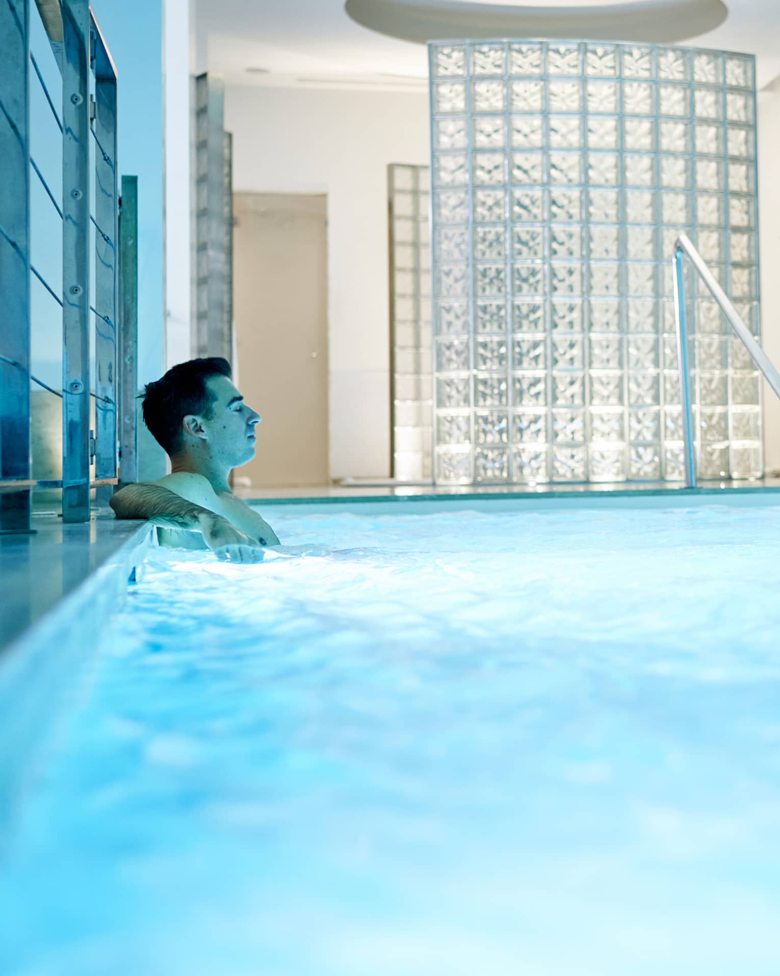 Man leans back in indoor pool with blue illuminated water