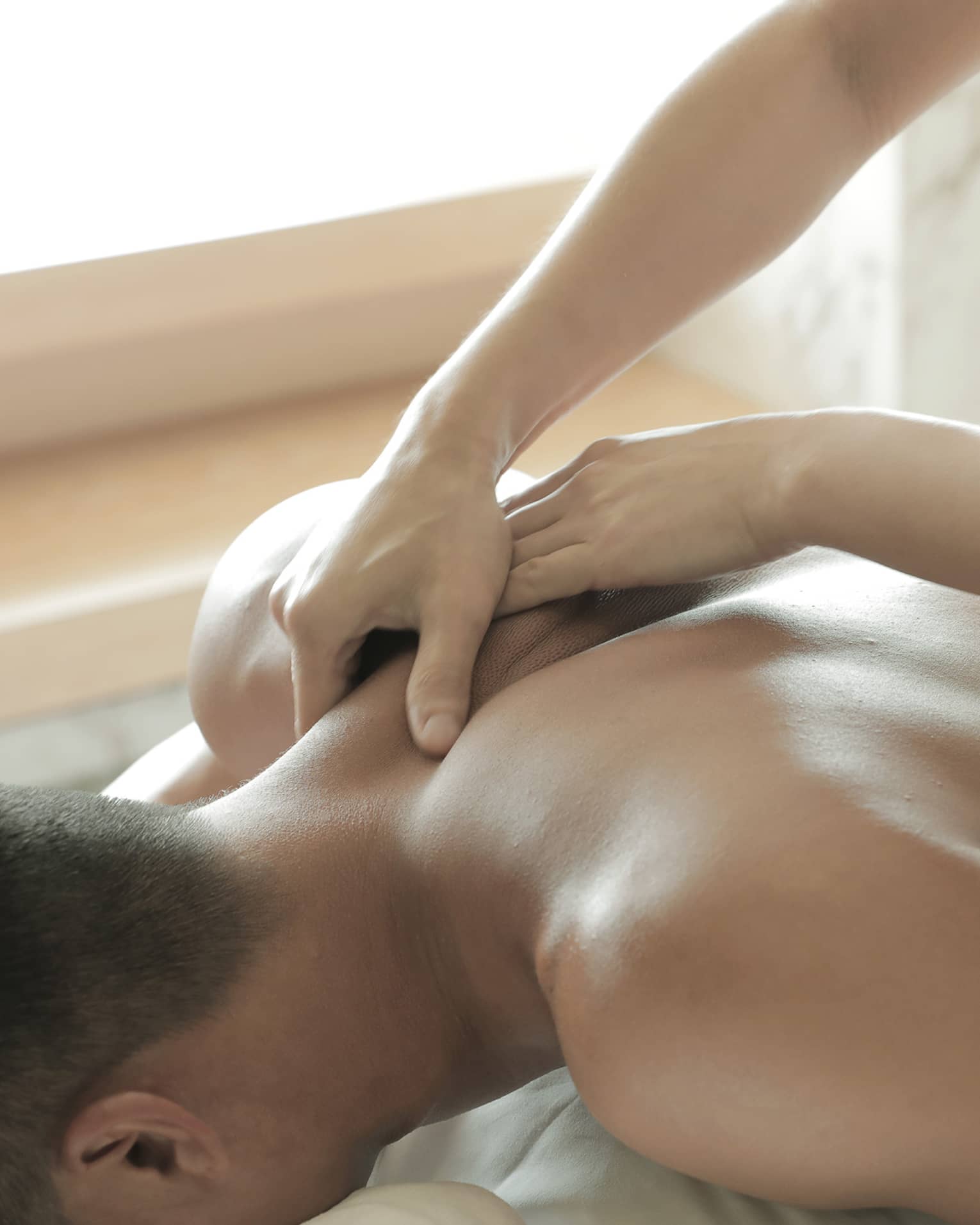 Spa masseuse massages man's bare back, shoulders