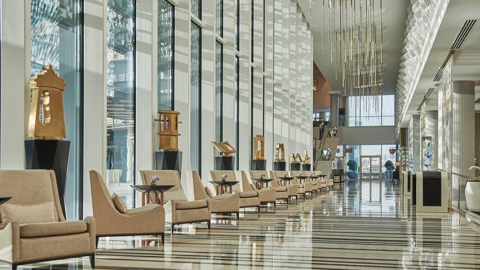 Hotel lobby with row of tan arm chairs, gold sculptures and floor-to-ceiling windows for natural light