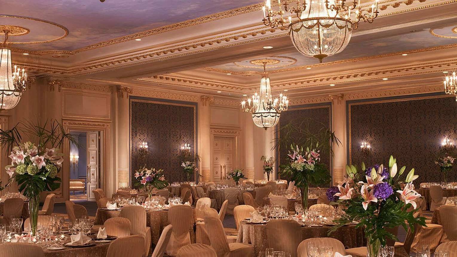 Elegantly set tables with gold tablecloths, flowers in ballroom with textured blue panels chandeliers 