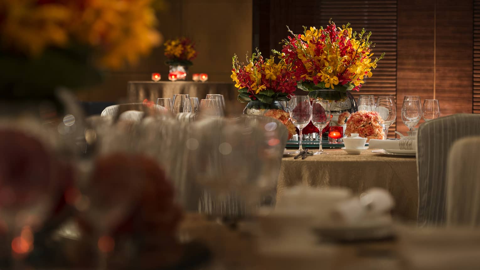 Orange and red flowers, candles on round banquet tables with gold linens