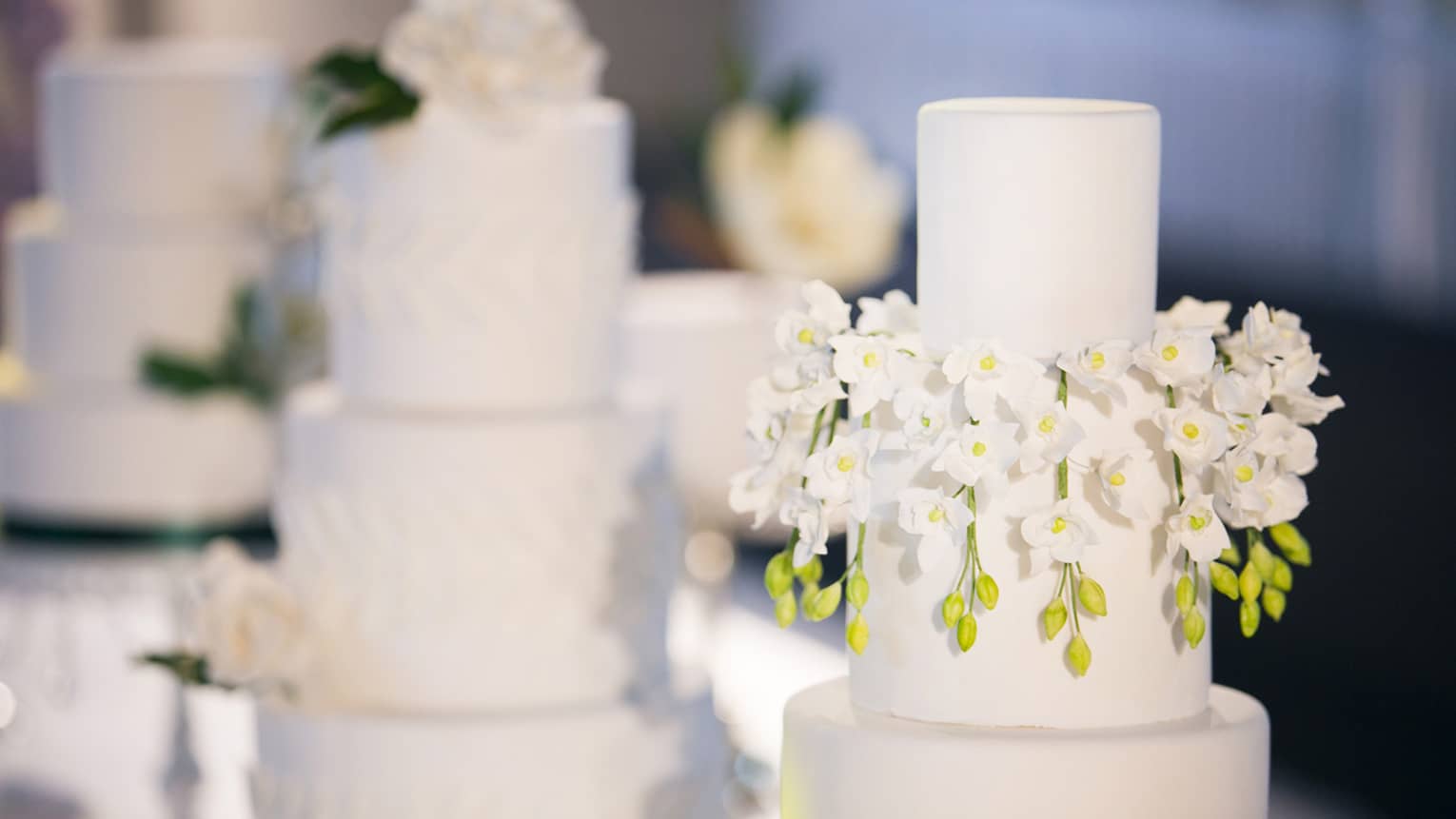 Three-tiered wedding cakes are each garnished with white florals 