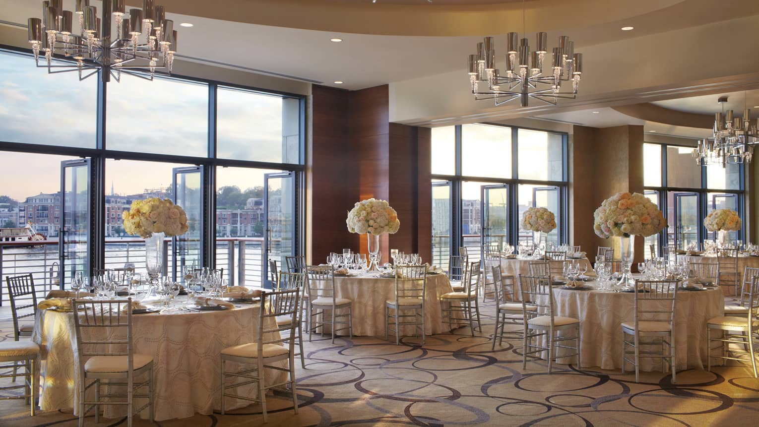 Ballroom with elegant round banquet tables by open air floor-to-ceiling windows overlooking Harbor East water
