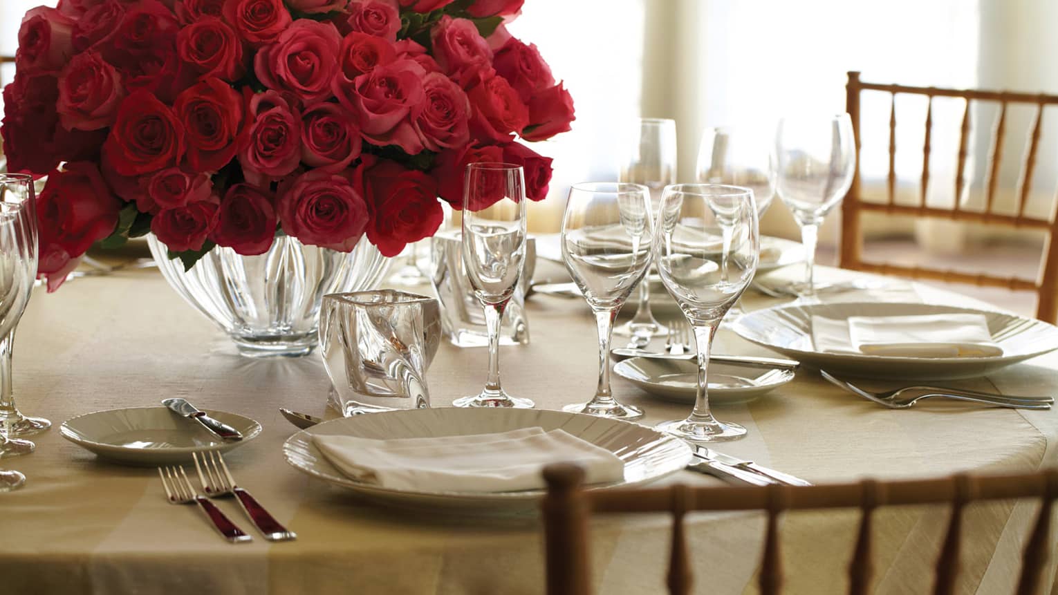 Banquet dining table place setting with plate, crystal glasses and vase with red rose bouquet
