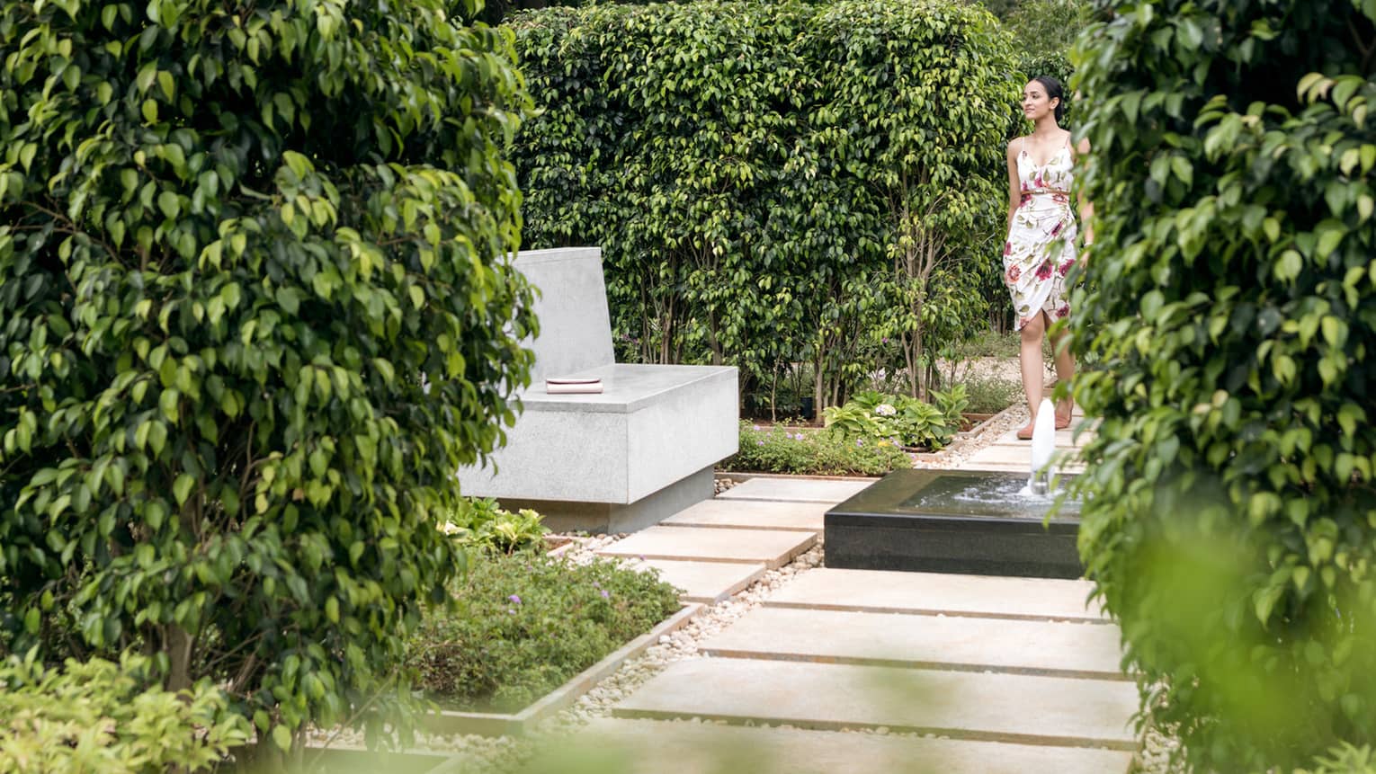 Woman walks along stone path with small fountain in garden
