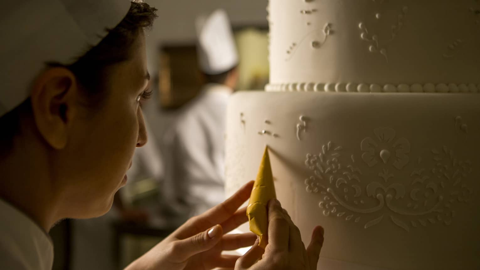 Pastry chef adds decorative details to tiered white wedding cake