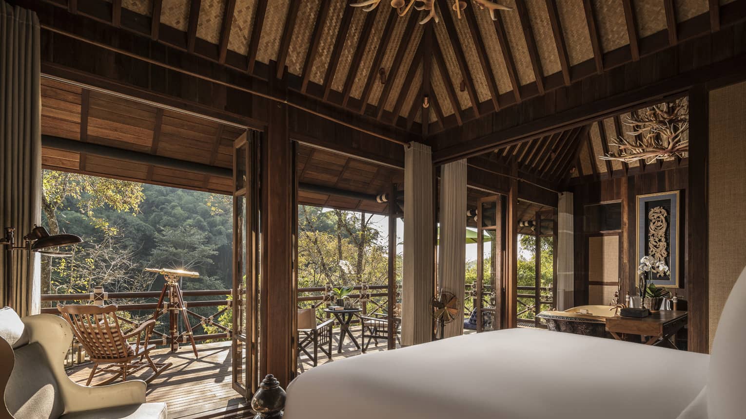 Hotel bed with white linens in open air cabin overlooking jungle