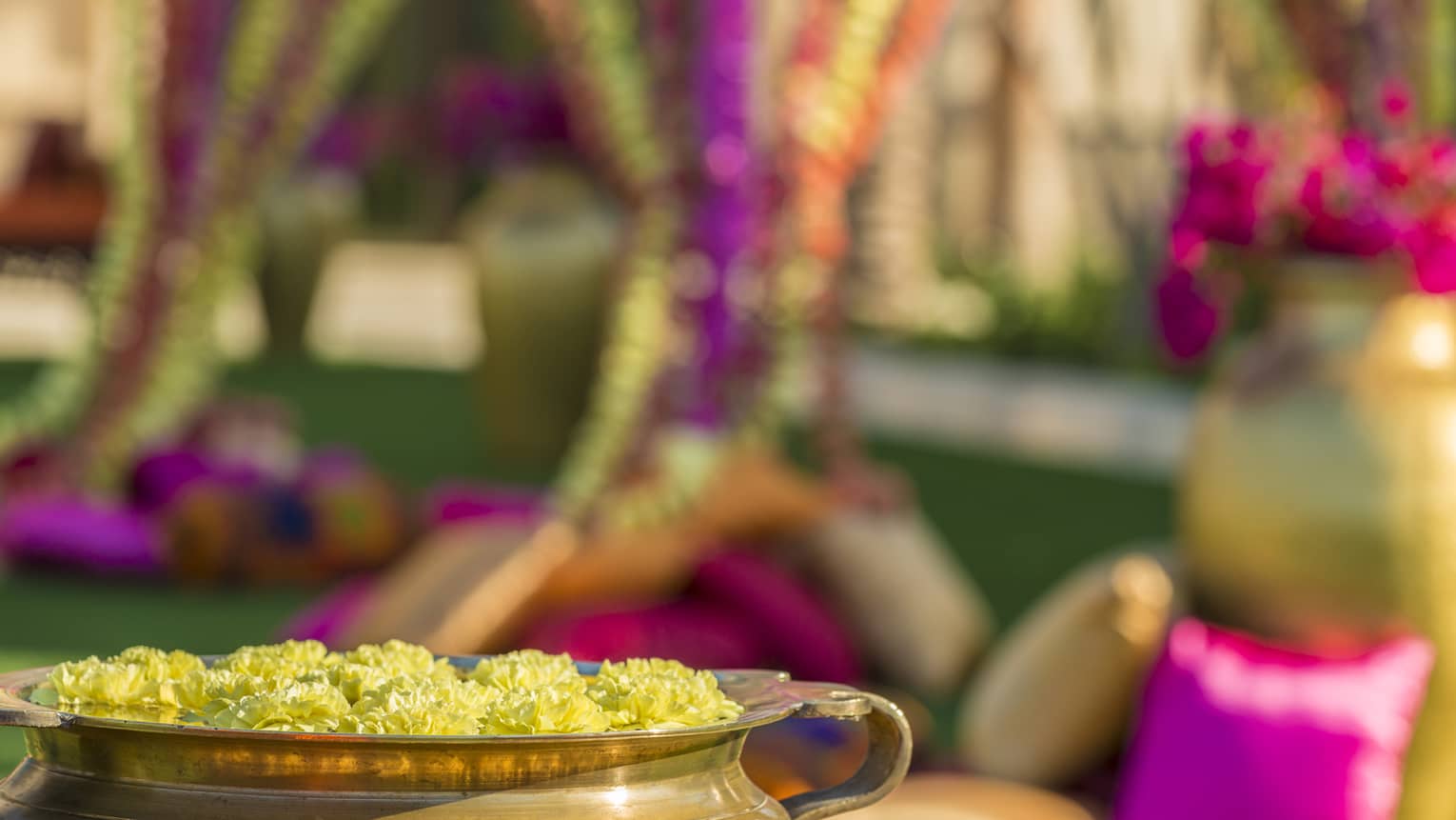 Copper pot with floating yellow flowers in front of brightly coloured cushions, garlands