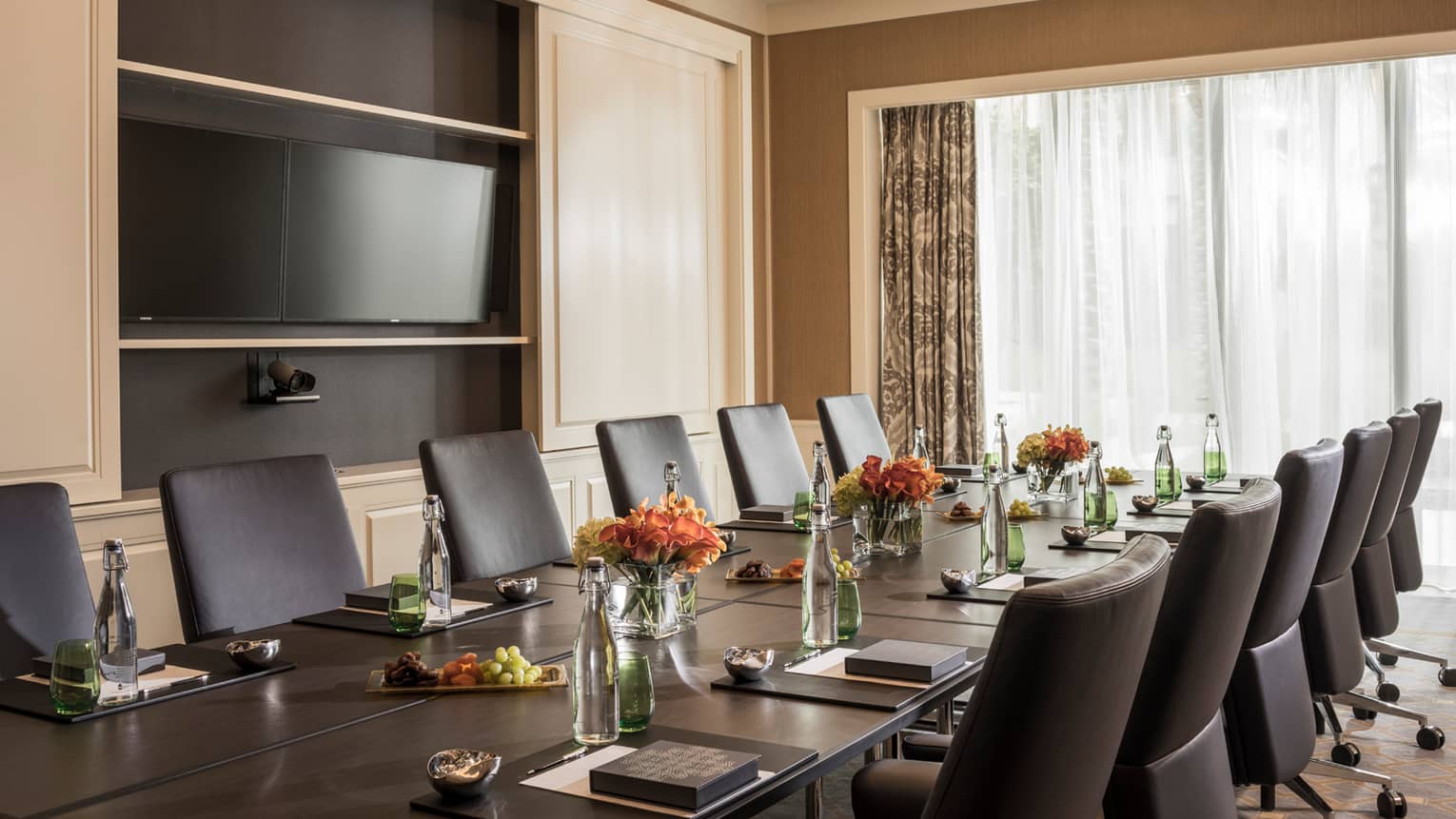 Long boardroom table set with glass bottles of water, flowers in bright meeting room