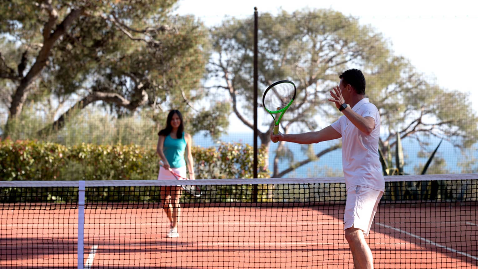 Man swings tennis racket, woman on other side of net