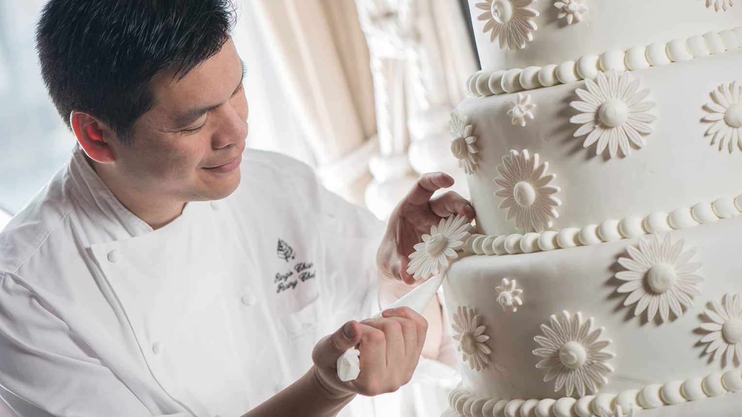 Pastry Chef Ringo Chan decorates icing of large tiered wedding cake