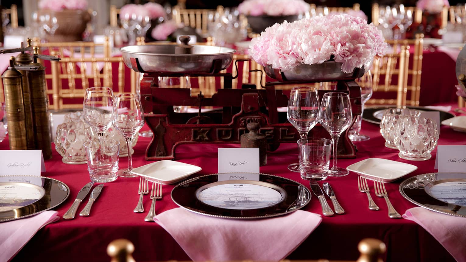 Close-up of banquet dining table with red tablecloth, pink flowers in antique iron holders 