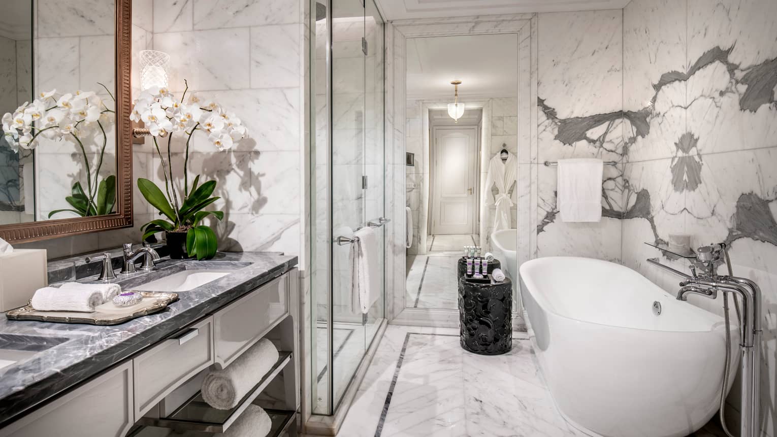 Modern bathroom with grey marble counters, white orchids in vase, glass shower