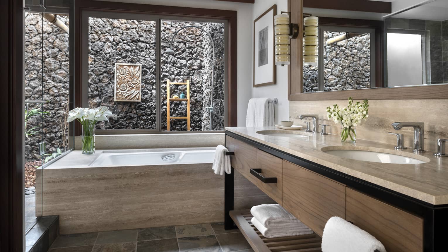 Bathroom with taupe marble vanity and tub, window looks out to outdoor stone shower