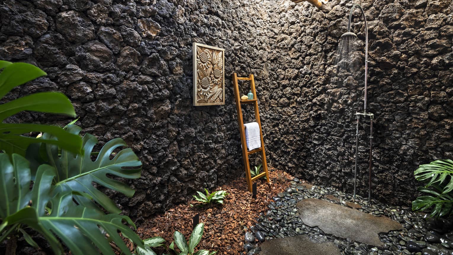 Outdoor shower with stone walls, teak ladder holding towel, greenery