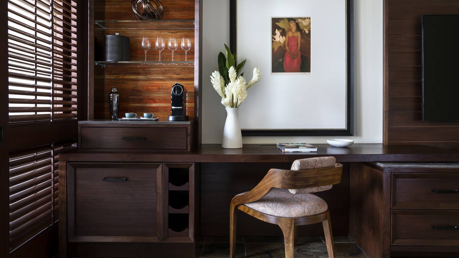 Built-in dark wood desk with wooden chair, vase of flowers, and glass shelves holding wine glasses