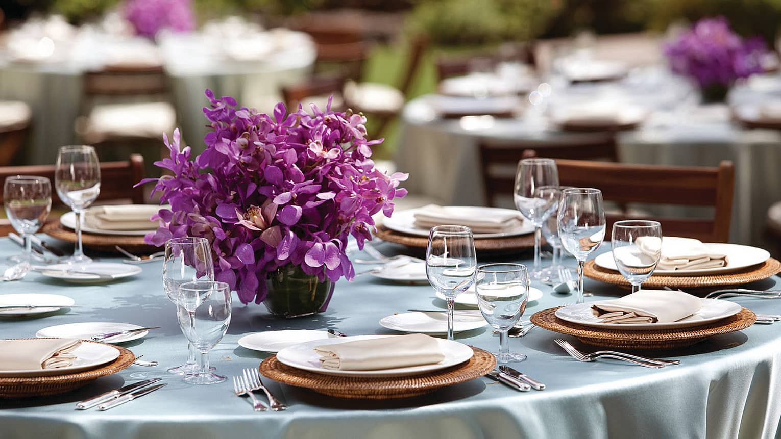Close-up of round outdoor dining table with place settings, purple flower centrepiece 