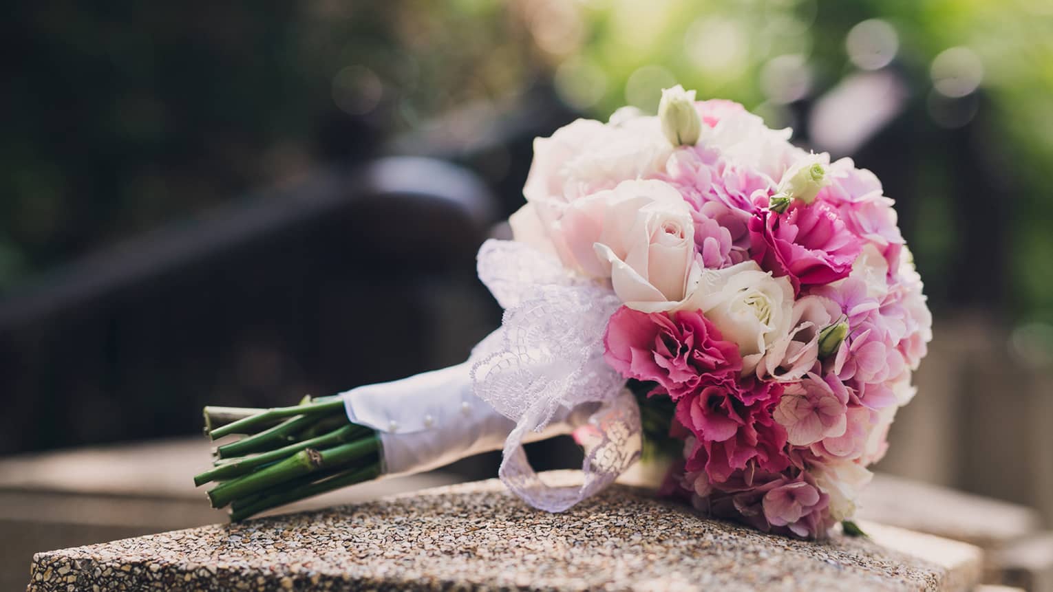 Pink and white floral wedding bouquet rests on stone pillar 