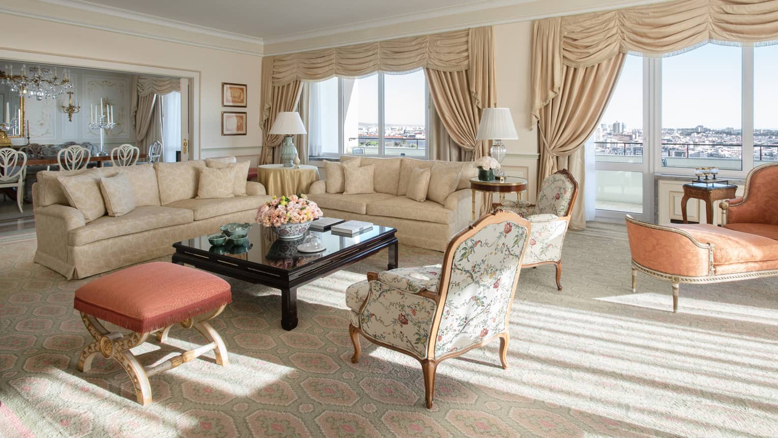 Presidential suite with two beige sofas, wing chairs, ottoman, orange chaise, tall windows with views