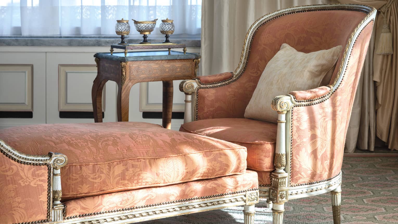 Close-up of formal orange chaise longue and side table beside curtained window