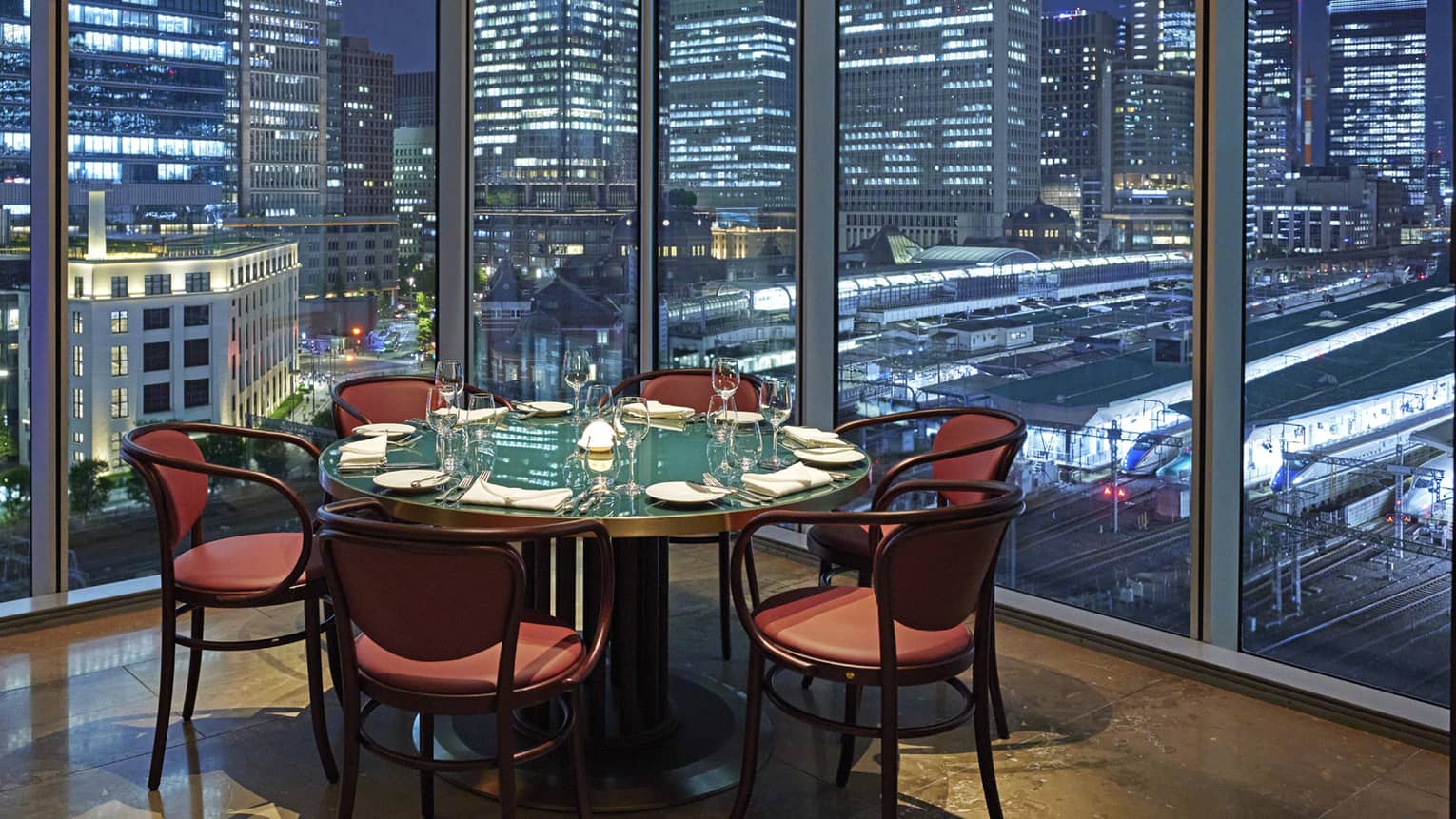 A round table and six chairs at Maison Marunouchi, floor-to-ceiling windows with views of downtown Tokyo at night
