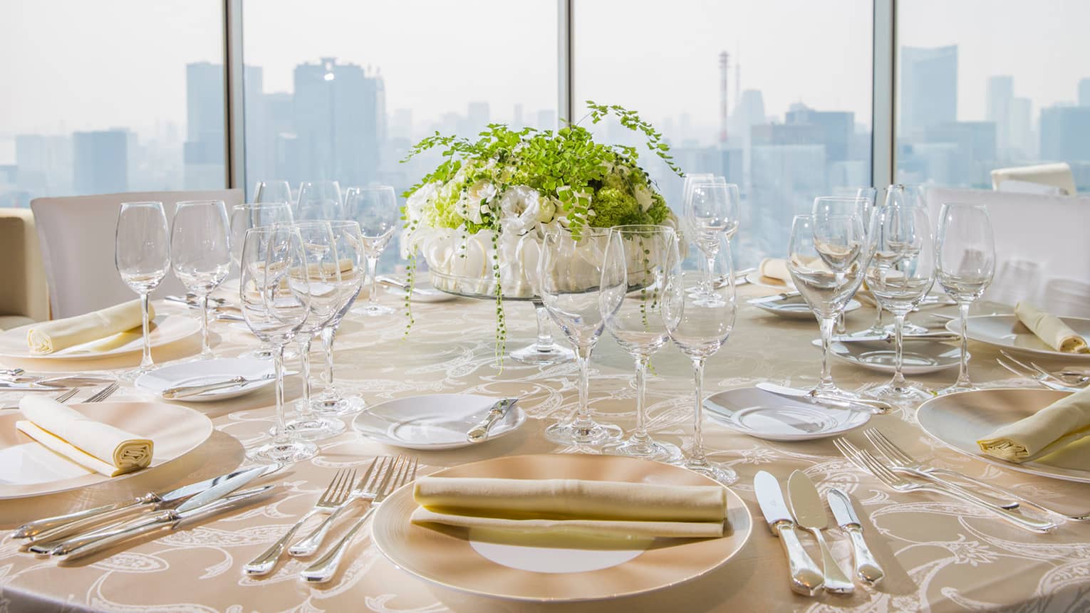 Table setting, rolled napkins on plates, glassware and floral arrangement on table by window