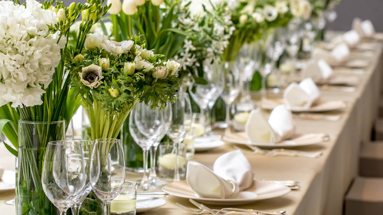 Close-up of long wedding dining table with wine glasses, white flowers in vases 