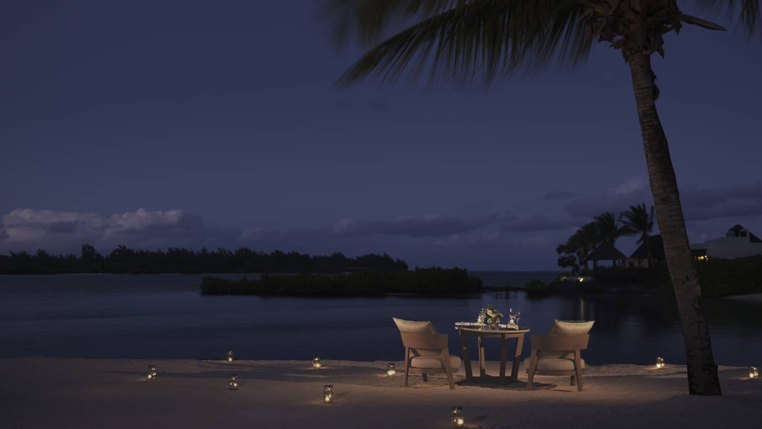 Dining table on beach, candles in sand, under starry night sky