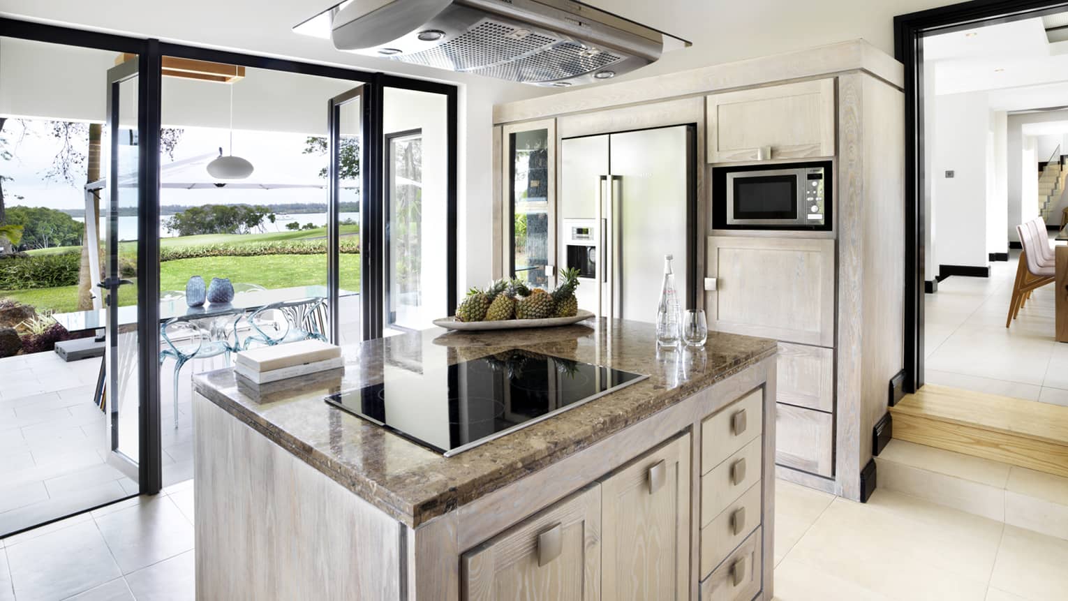 Stove range on marble island in bright, modern kitchen with open glass walls