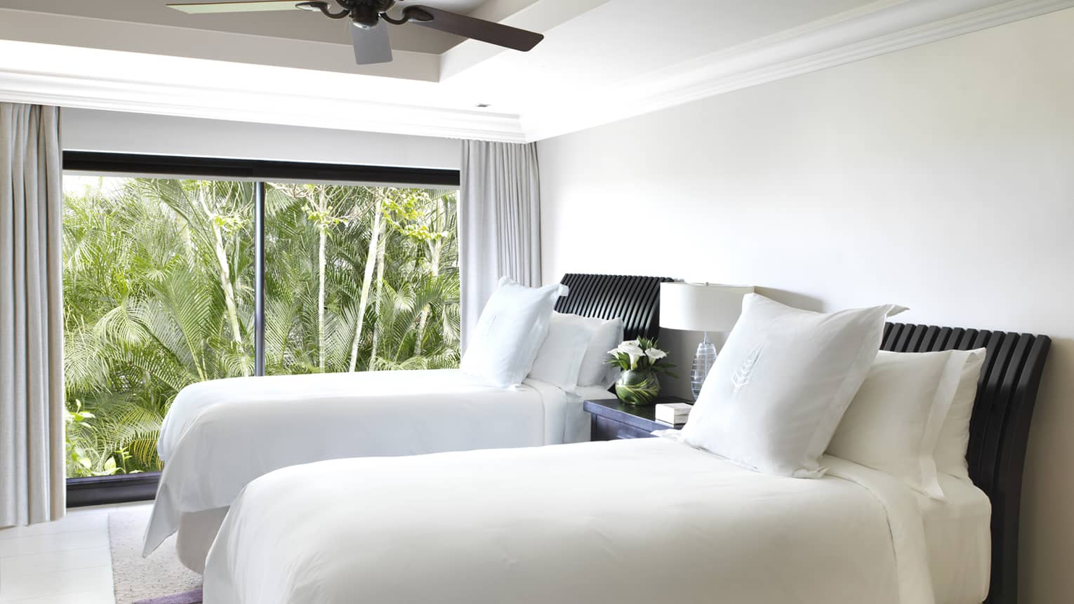 Two single beds with white linens, pillows in bright room by floor-to-ceiling window