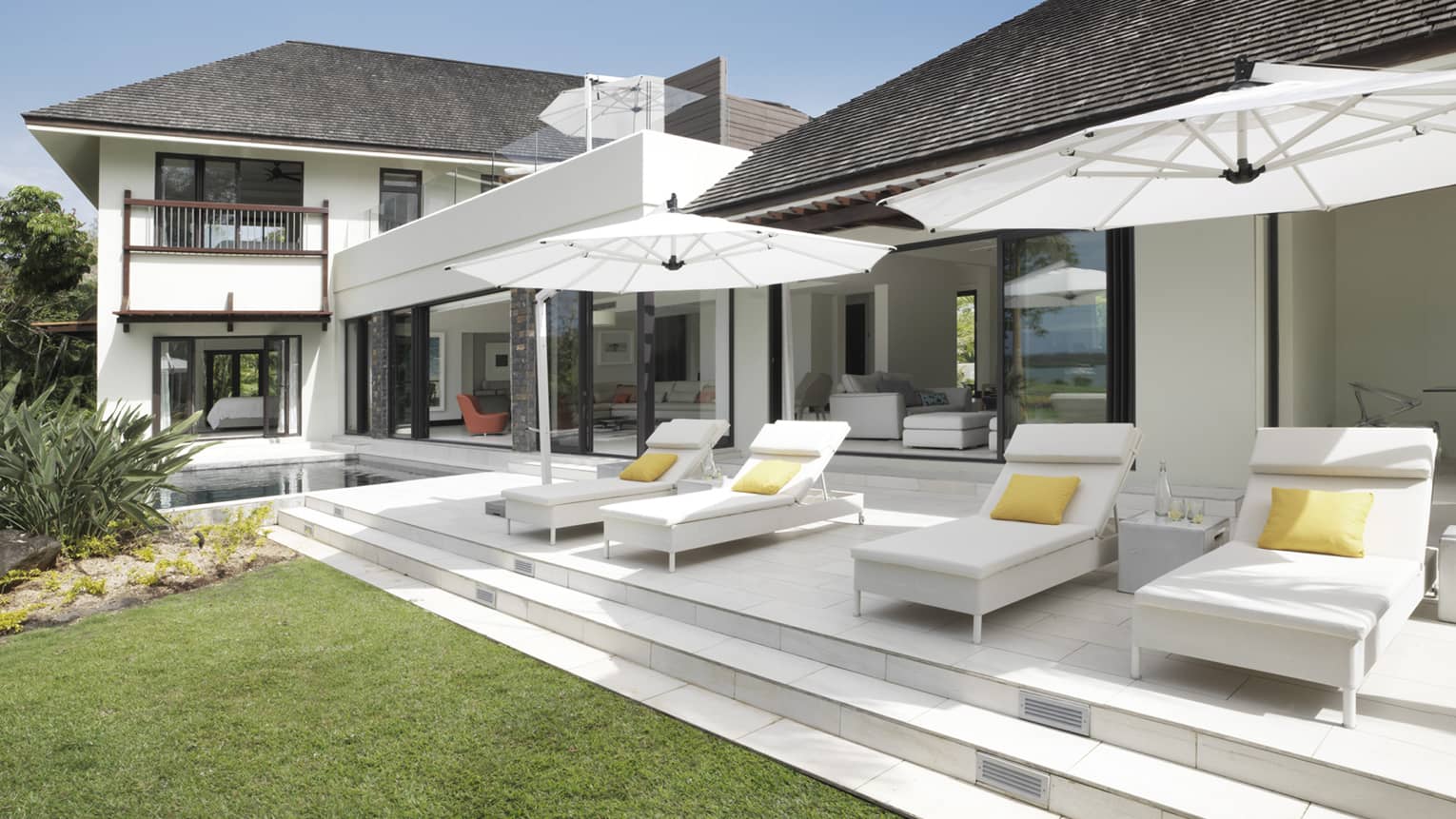 White lounge chairs under umbrellas on patio in front of large white two-storey villa