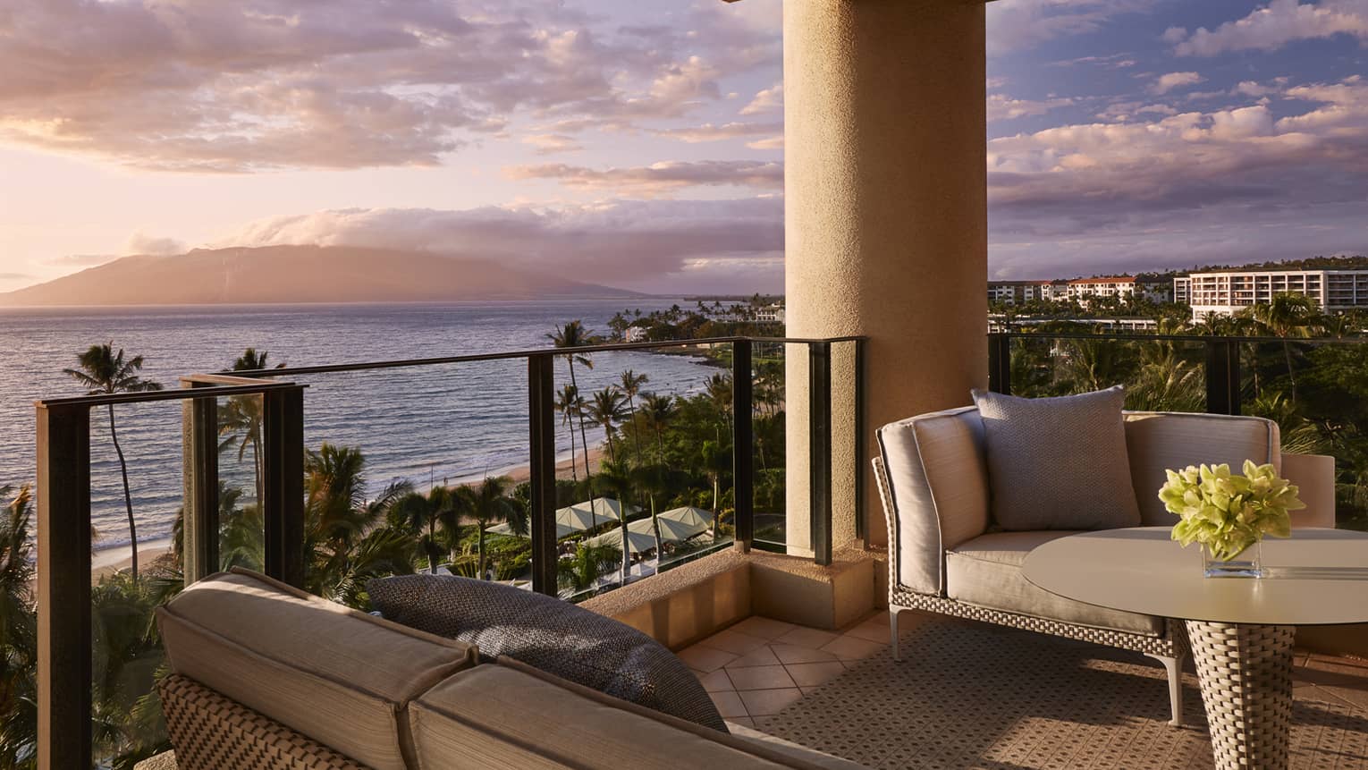 Outdoor terrace with sofa, arm chair, glass railing, looking out to sunset over ocean