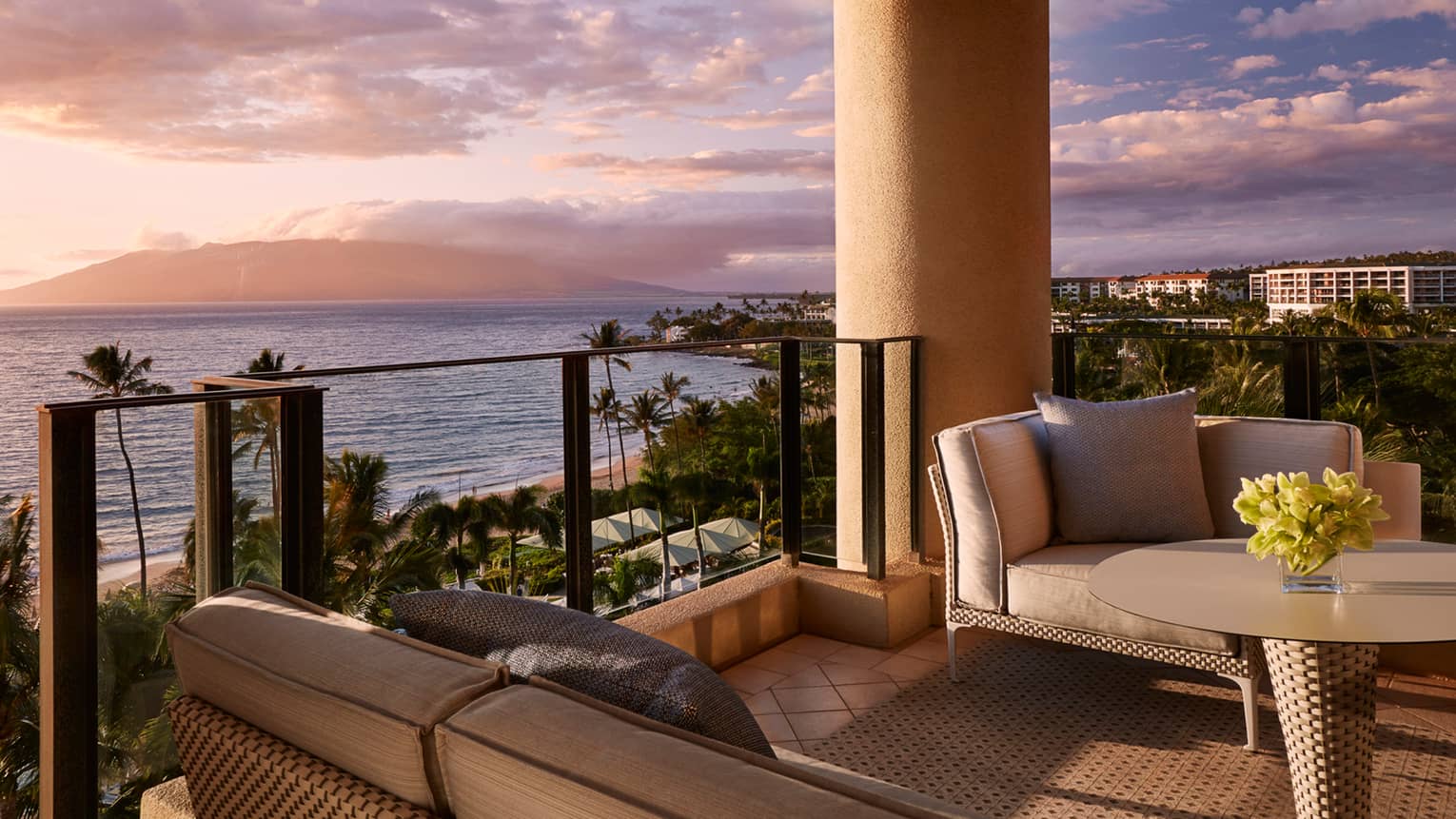 Balcony with wicker patio furniture, brown cushions in front of ocean view at sunset