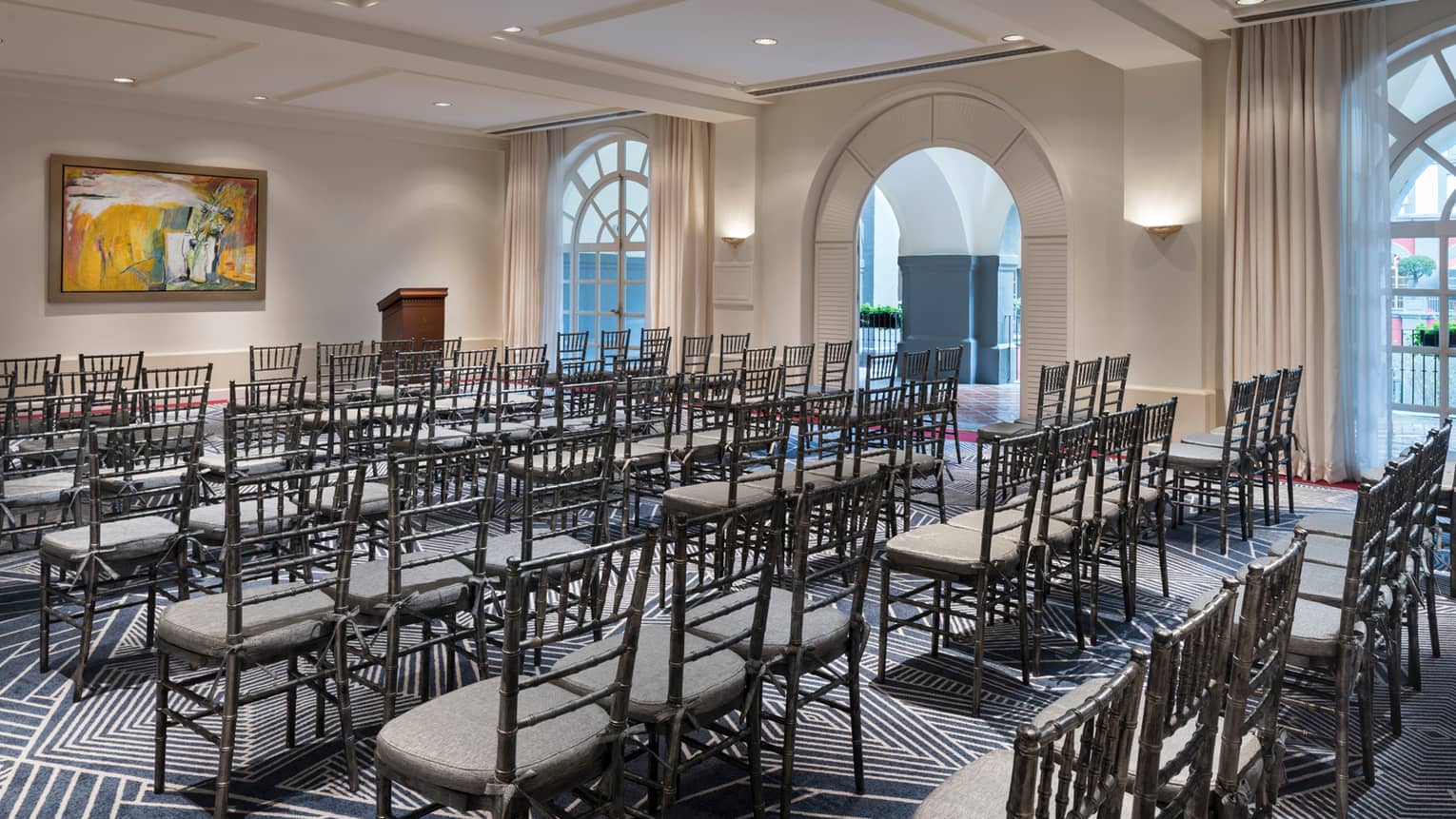 Conference, rows of chairs along arched windows facing wall with colourful orange paining 