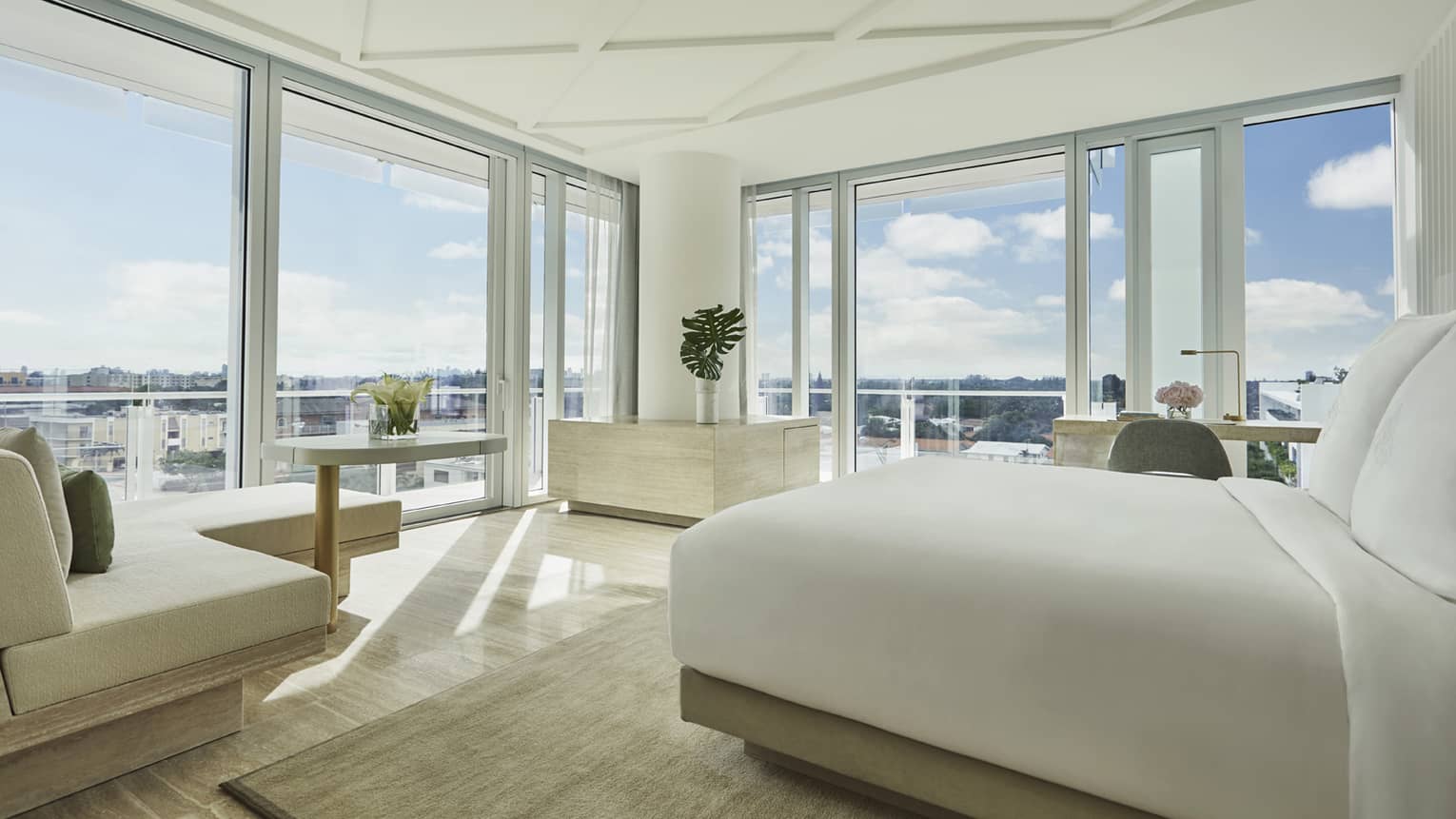 Sunset Studio Suite with modern white bed and chaise, and floor-to-ceiling windows with expansive views