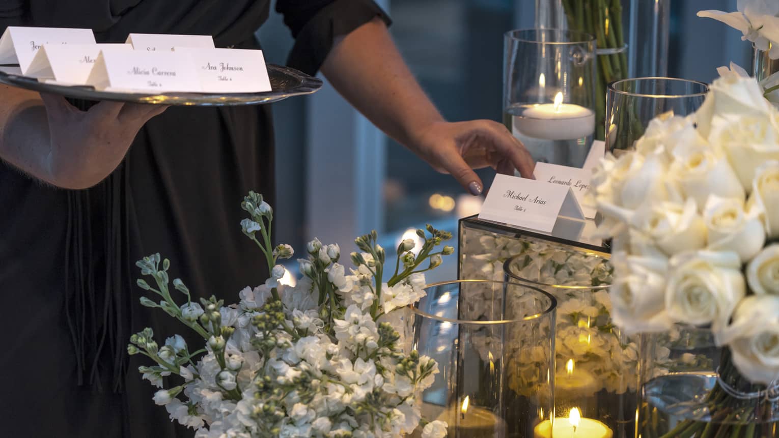 Event staff with tray places name cards on elegant banquet table with white flowers, candles