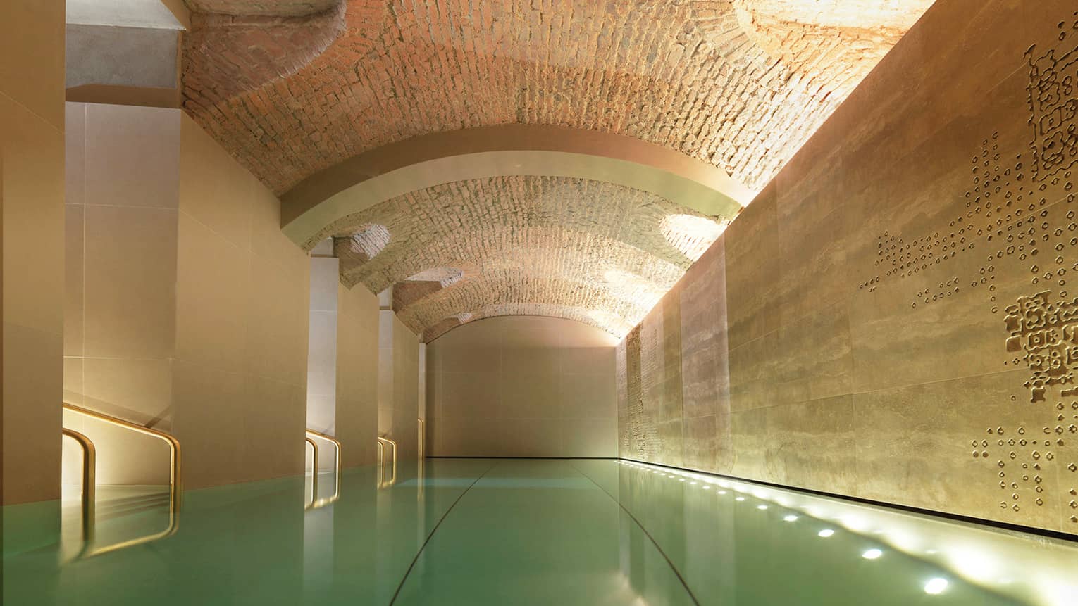 Indoor lap swimming pool with gold railings under curved stone ceiling