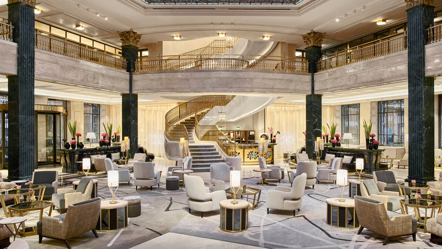 Hotel lobby featuring arm chairs and low tables, with large spiral staircase in the background