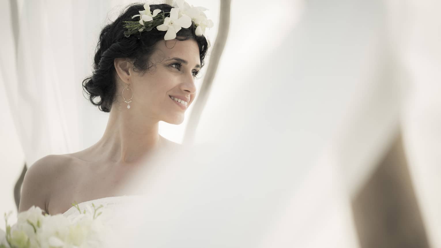 Smiling bride with flowers in hair behind white linen