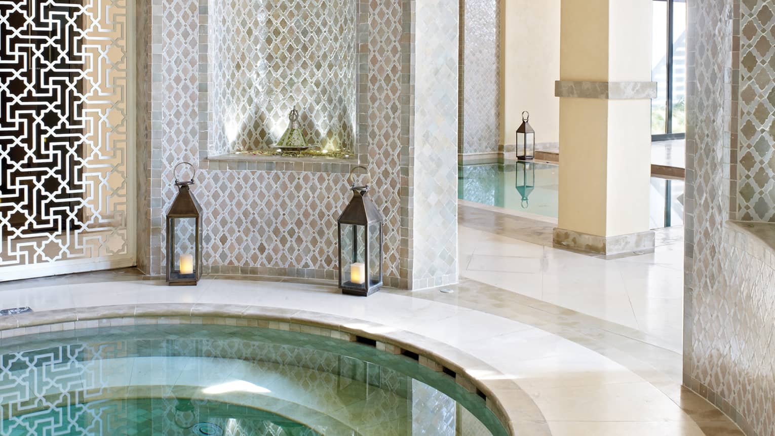 Small round whirlpool tub surrounded by decorative white detail wall, lanterns