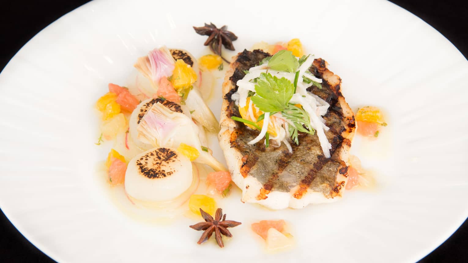 Grilled white fish filet and three seared scallops on plate with herbs, vegetable garnish