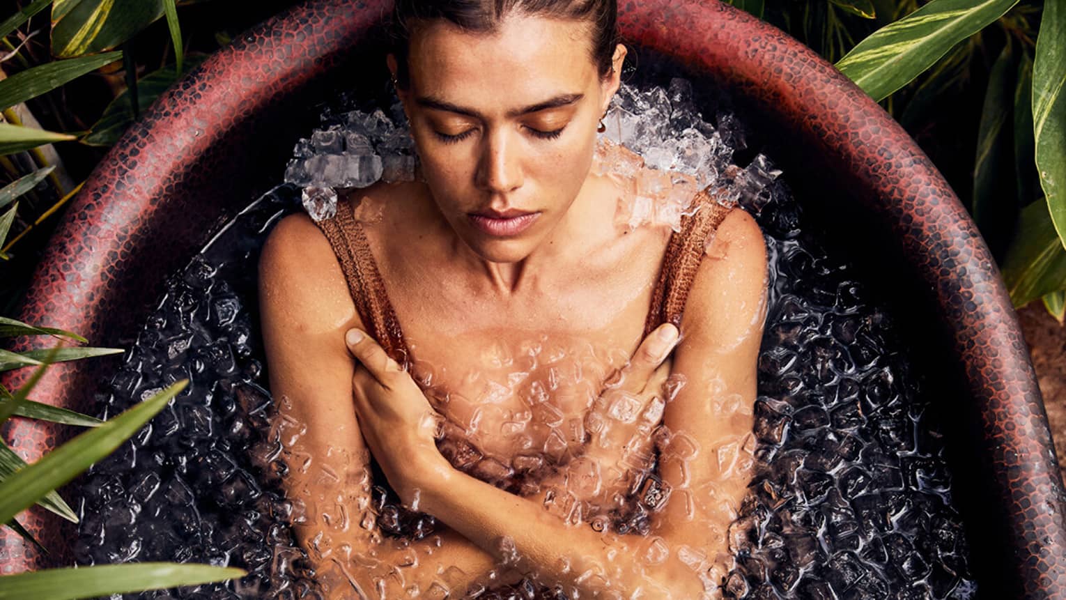 A woman submerged in an ice bath surrounded by plants.