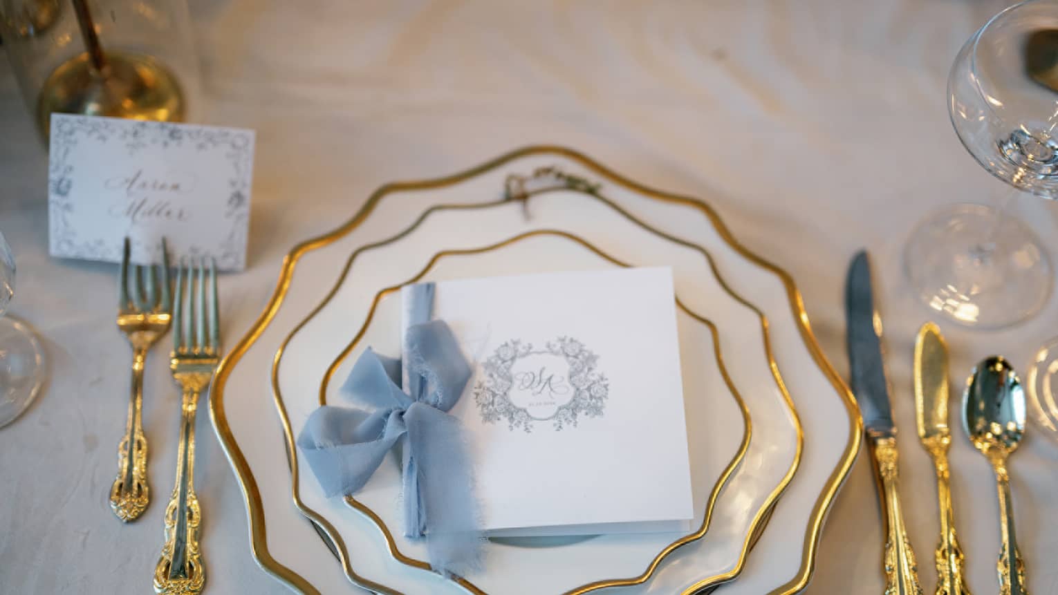Gold and white plates with gold utensils and wedding card.
