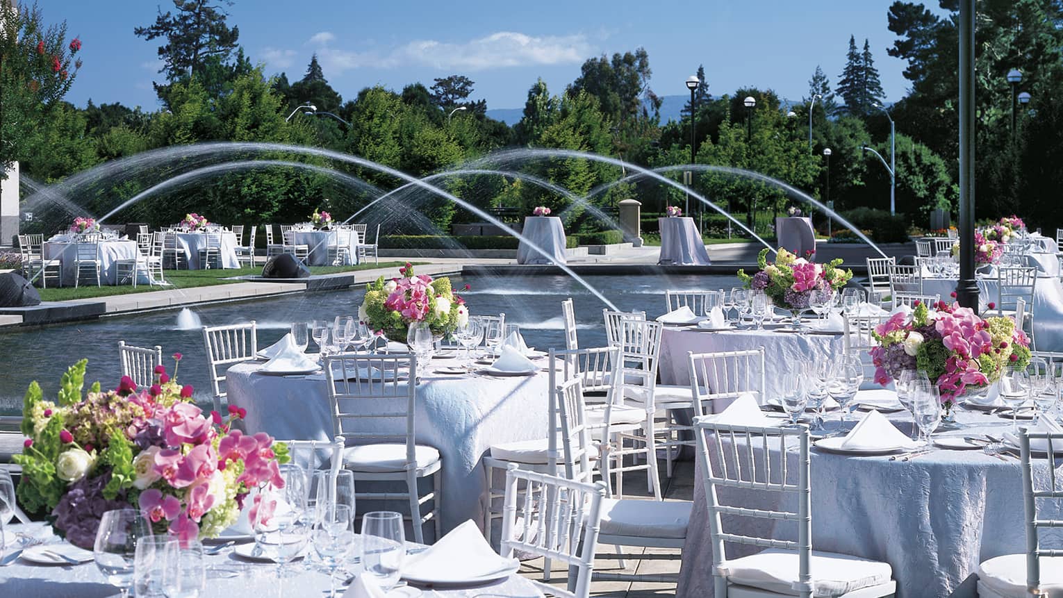 Outdoor banquet tables with white linens, flowers around courtyard fountain